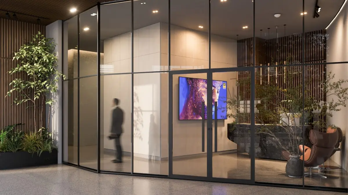 41 Business District – Lobby hinter einer schwarz gerahmten Glaswand mit Pflanzen und Wandbildschirm