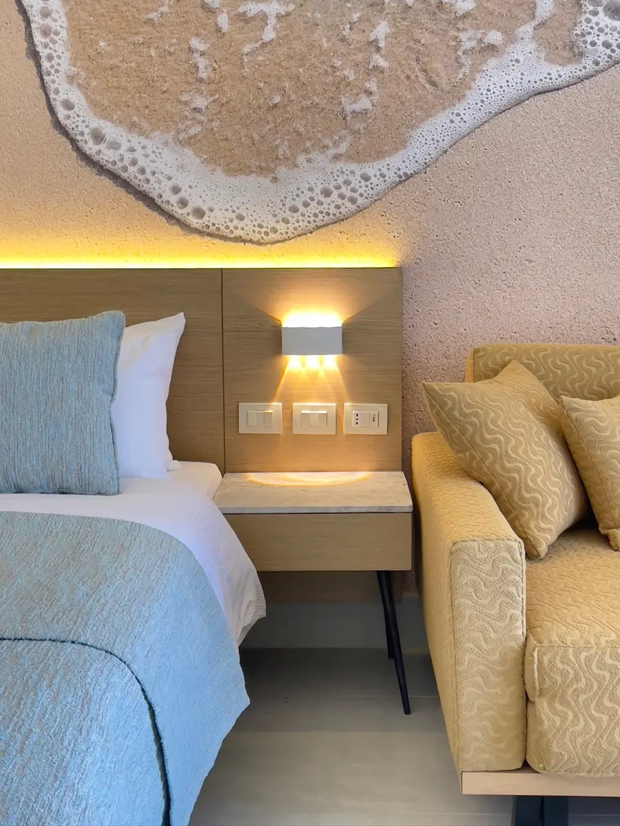Amwaj Resort Rooms Extension – Bedside detail with timber headboard, wall light and wave relief above