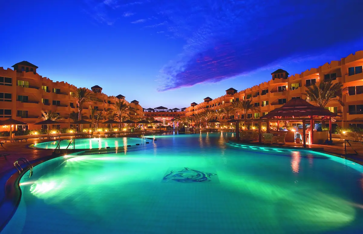 Amwaj Soma Hotel & Spa – مسبح البحيرة بلونه الفيروزي المضيء عند الغسق مع فسيفساء دلفين وأجنحة مضاءة