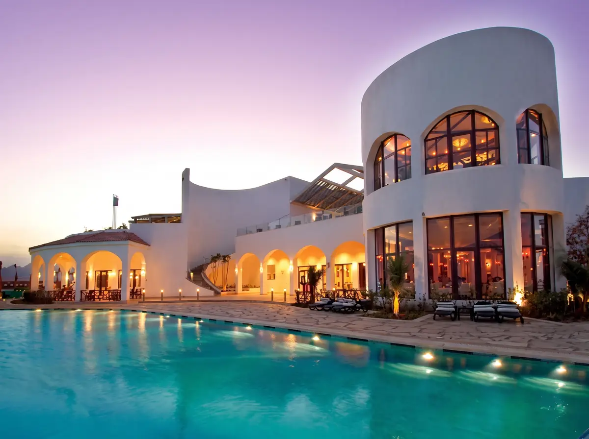 Blue Bay Resort Thalassotherapy Spa – Curved white spa building with lit arched windows above the pool at dusk