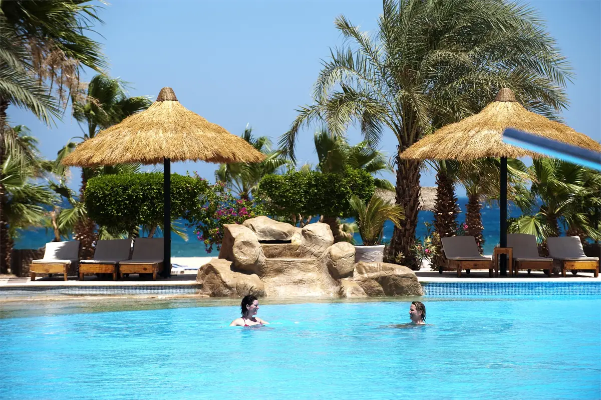 Lotus Bay Resort Renovation – Guests swimming beside a sculpted rock feature, with thatched parasols and palms