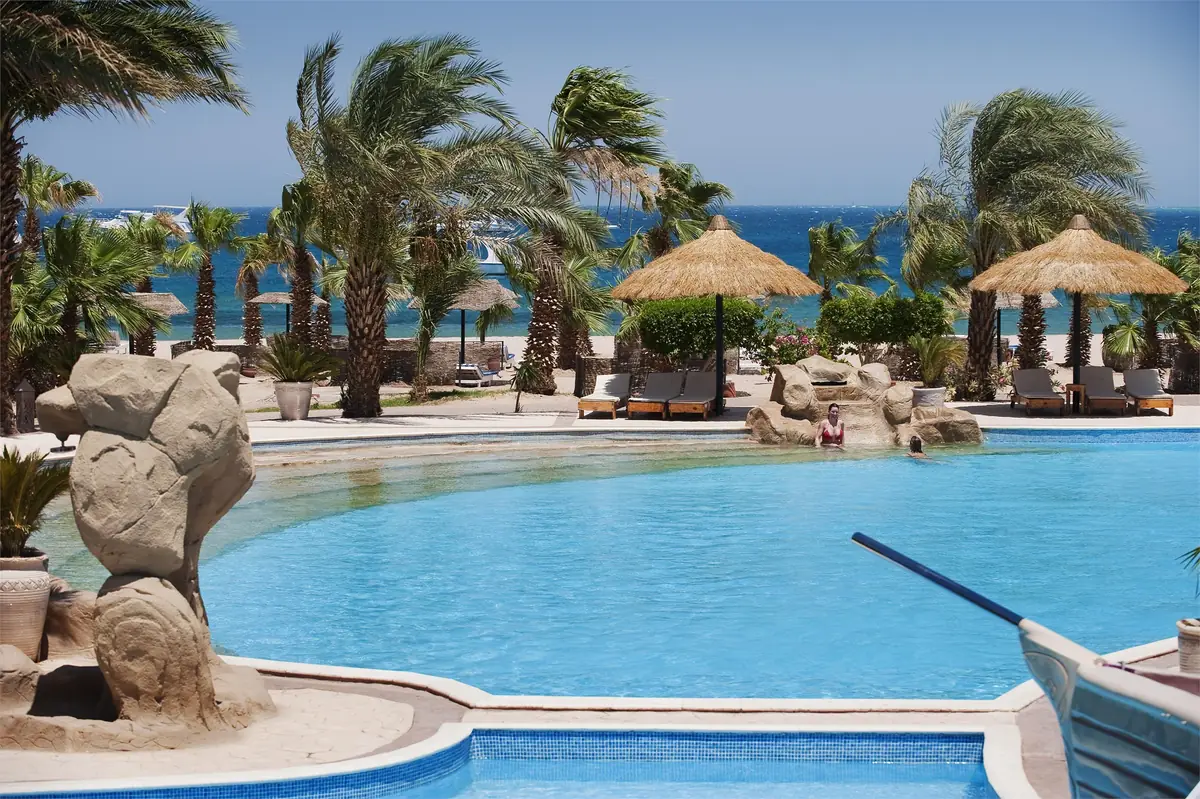 Lotus Bay Resort Renovation – Free-form pool with a carved rock figure and windswept palms by the sea