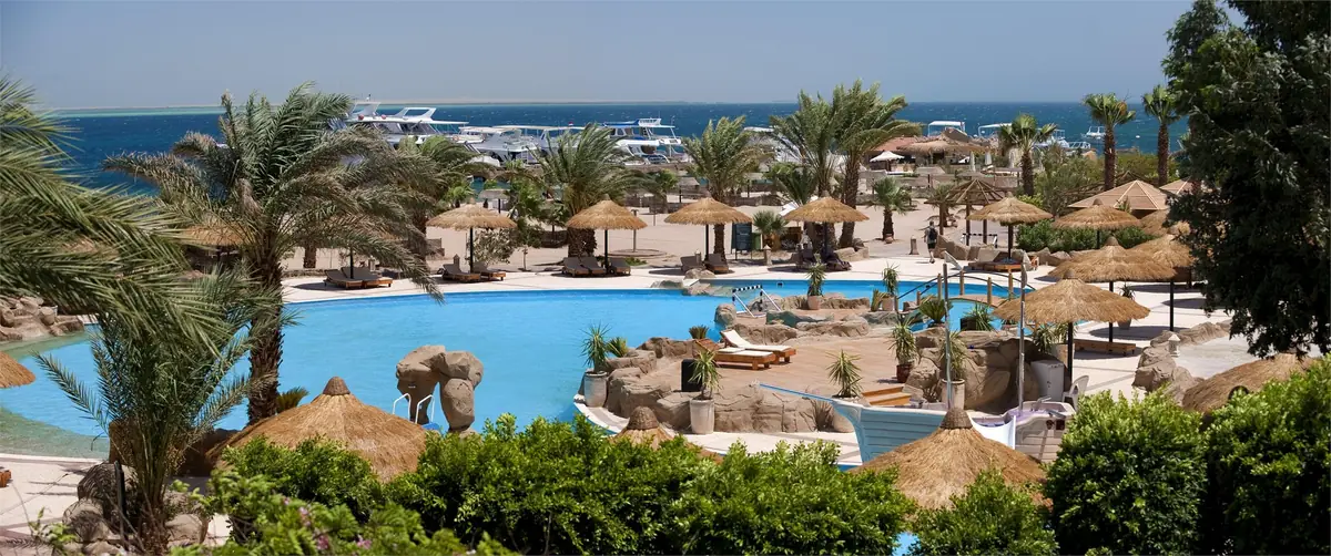 Lotus Bay Resort Renovation – Panoramic view of the main pool and thatched parasols, with boats offshore