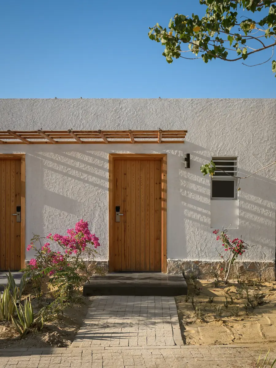 Marmarica Boutique cabanas – White textured cabana wall with timber doors, pergola and bougainvillea