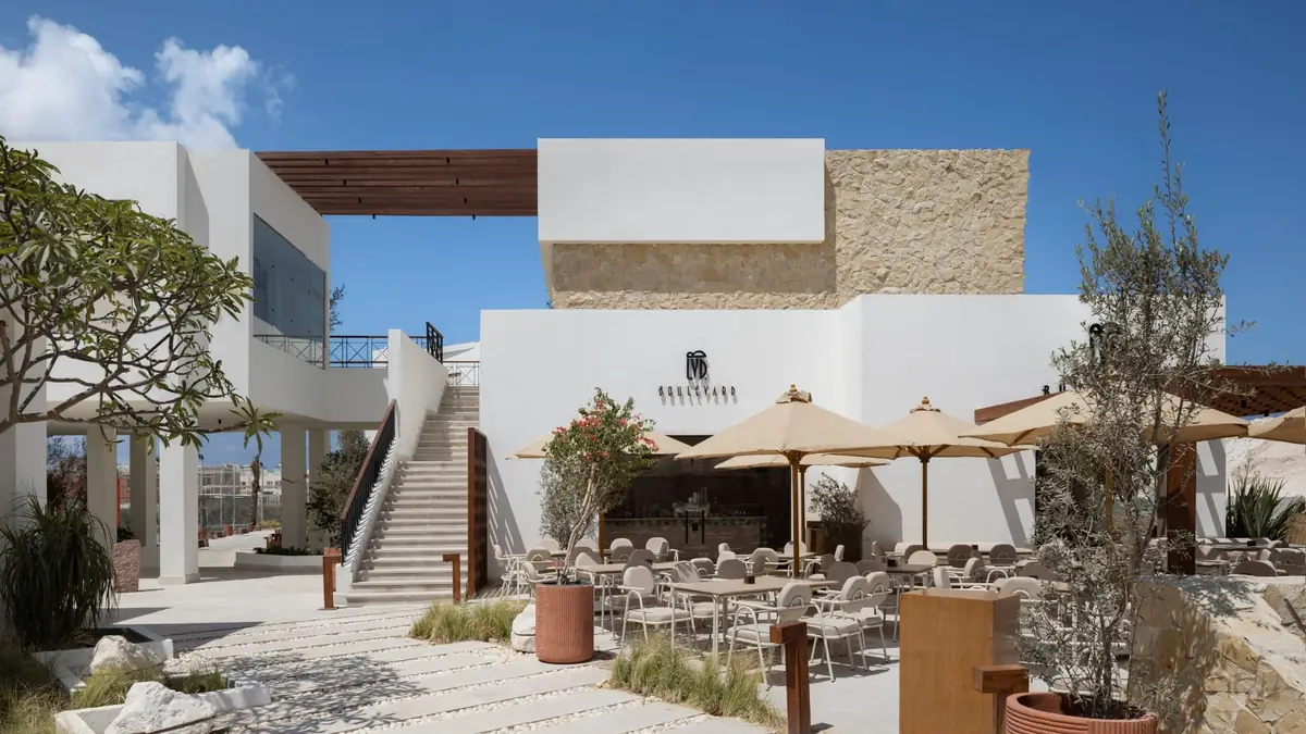 Masyaf Ras Al-Hekma – Restaurant terrace with canvas parasols below a stone-clad volume and open stair