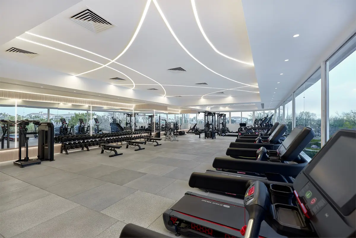 Move – Green Heights Sports Complex – Training floor with treadmills in front and free weights beyond, under curving light lines