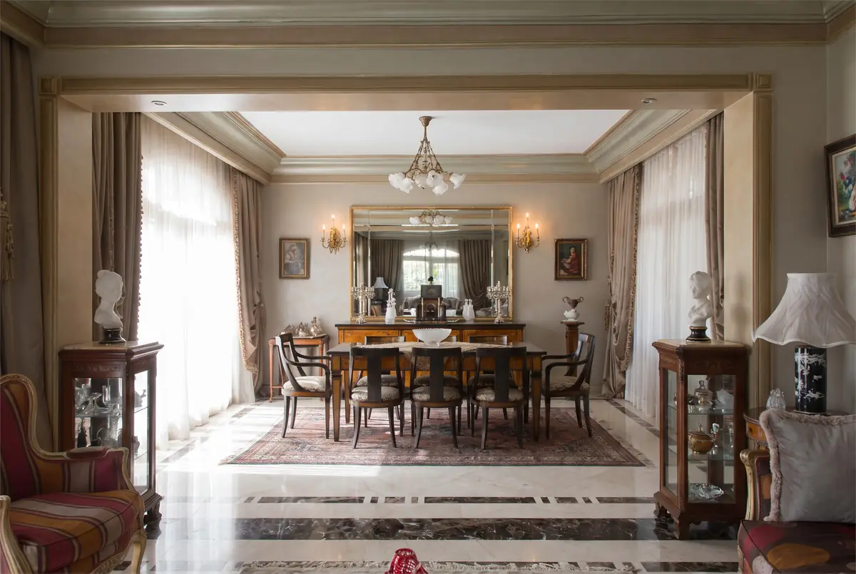 Mrs. M.A.'s Villa – Formal dining room through a moulded opening, with chandelier and inlaid stone floor