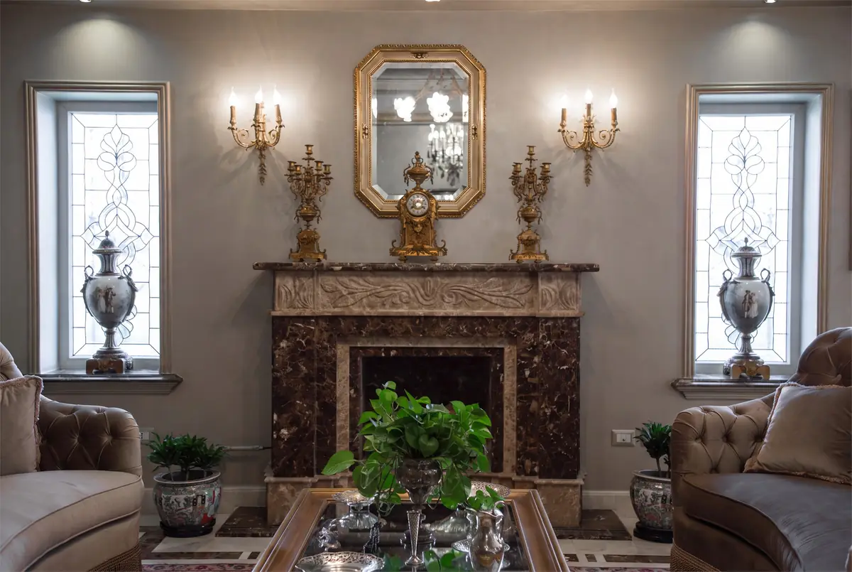Mrs. M.A.'s Villa – Reception room with carved marble fireplace between leaded-glass windows and gilded sconces