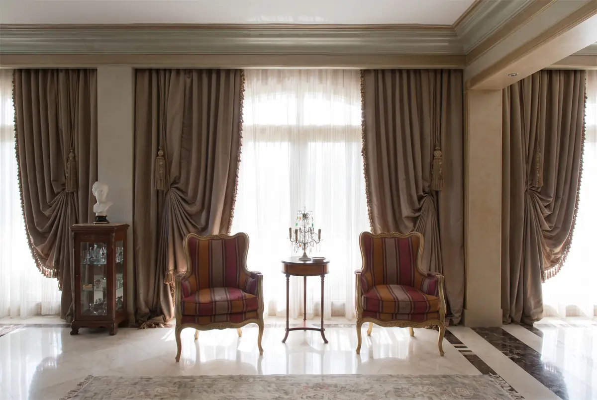 Mrs. M.A.'s Villa – Pair of striped armchairs before tall windows with draped, tasselled curtains
