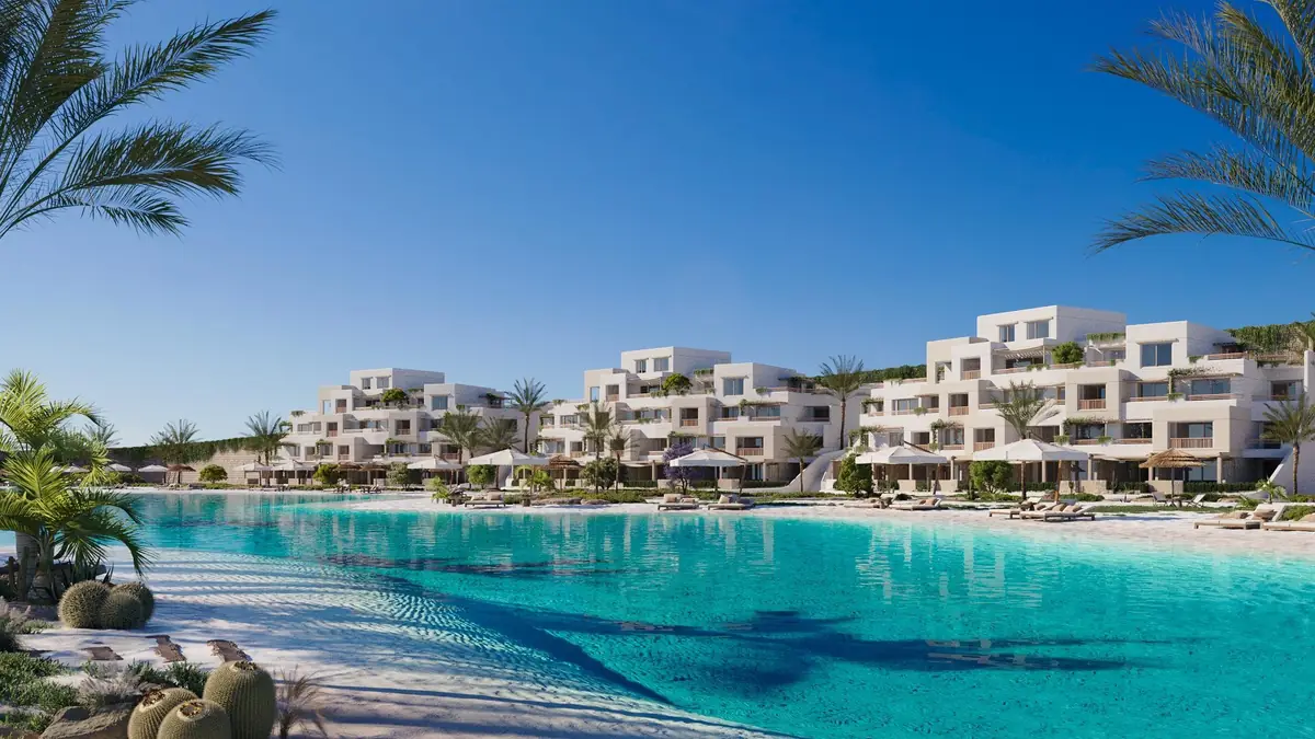 Oyster at Masyaf – Turquoise lagoon framed by palms and cacti, facing terraced white apartment blocks