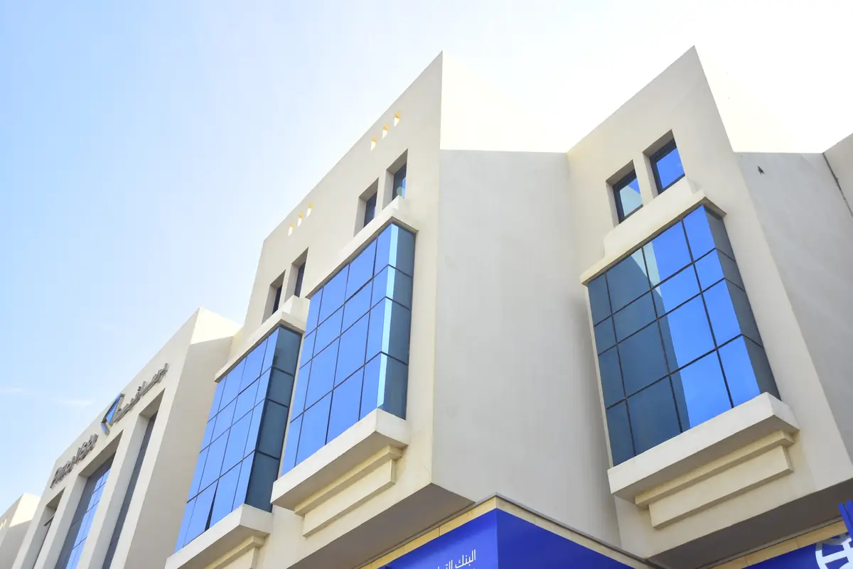 Prima Vista – Medical Office & Commercial Mall – Upward view of blue-glass bays in warm cream plaster with small parapet openings