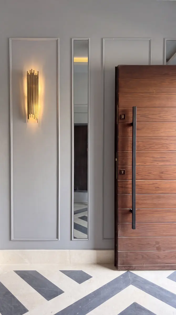 Prof. Dr. M.H. & Prof. Dr. Y.K.'s Villa – Walnut pivot door beside a brass sconce and mirror strip on a panelled wall