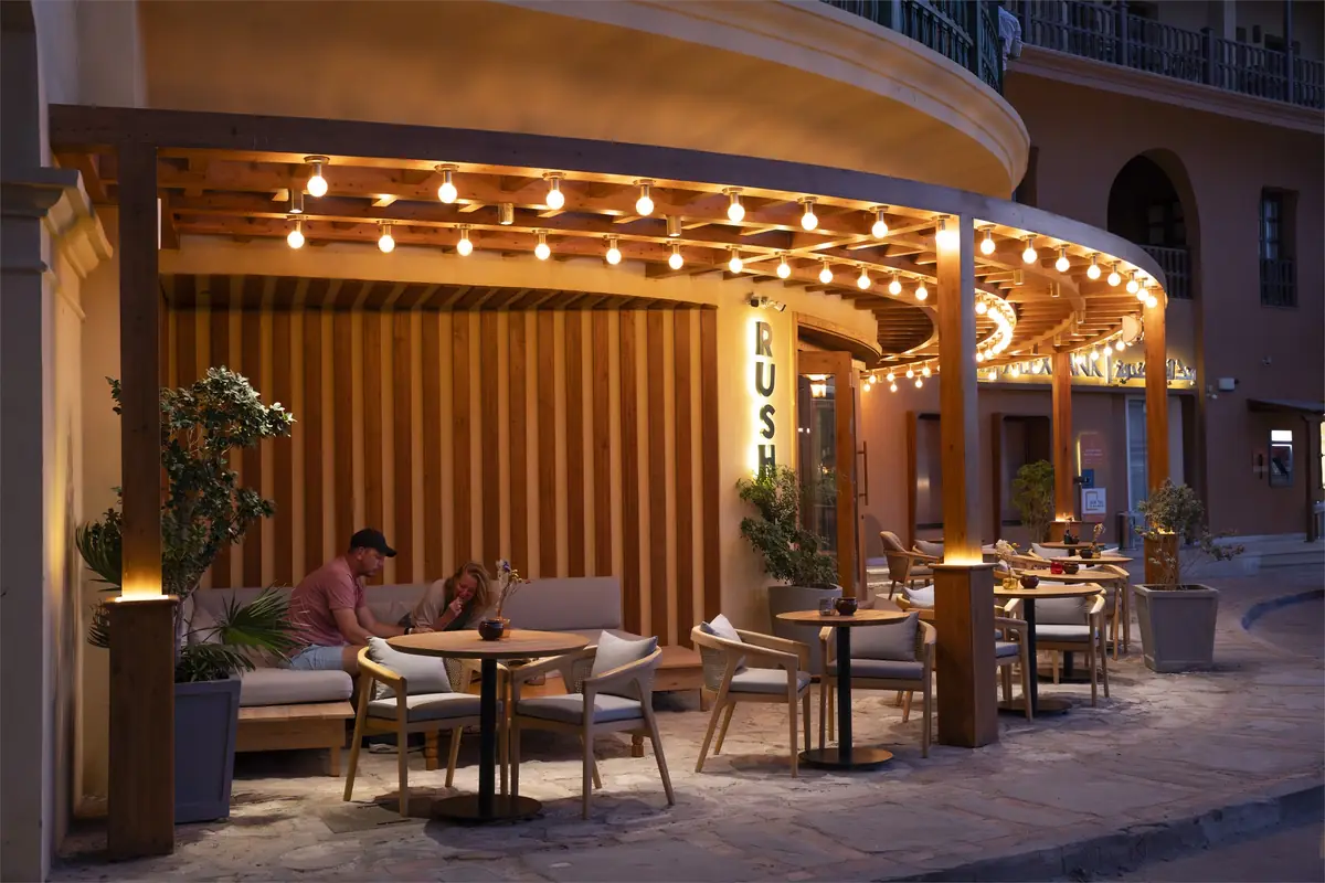 Rush – Sports Bar – Gäste auf der Pergola-Terrasse neben einer Holzlamellenwand und einer Loungebank