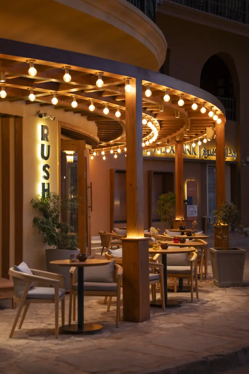 Rush – Sports Bar – Angestrahlte Holzstützen entlang der geschwungenen Terrasse mit Lichterketten bei Nacht