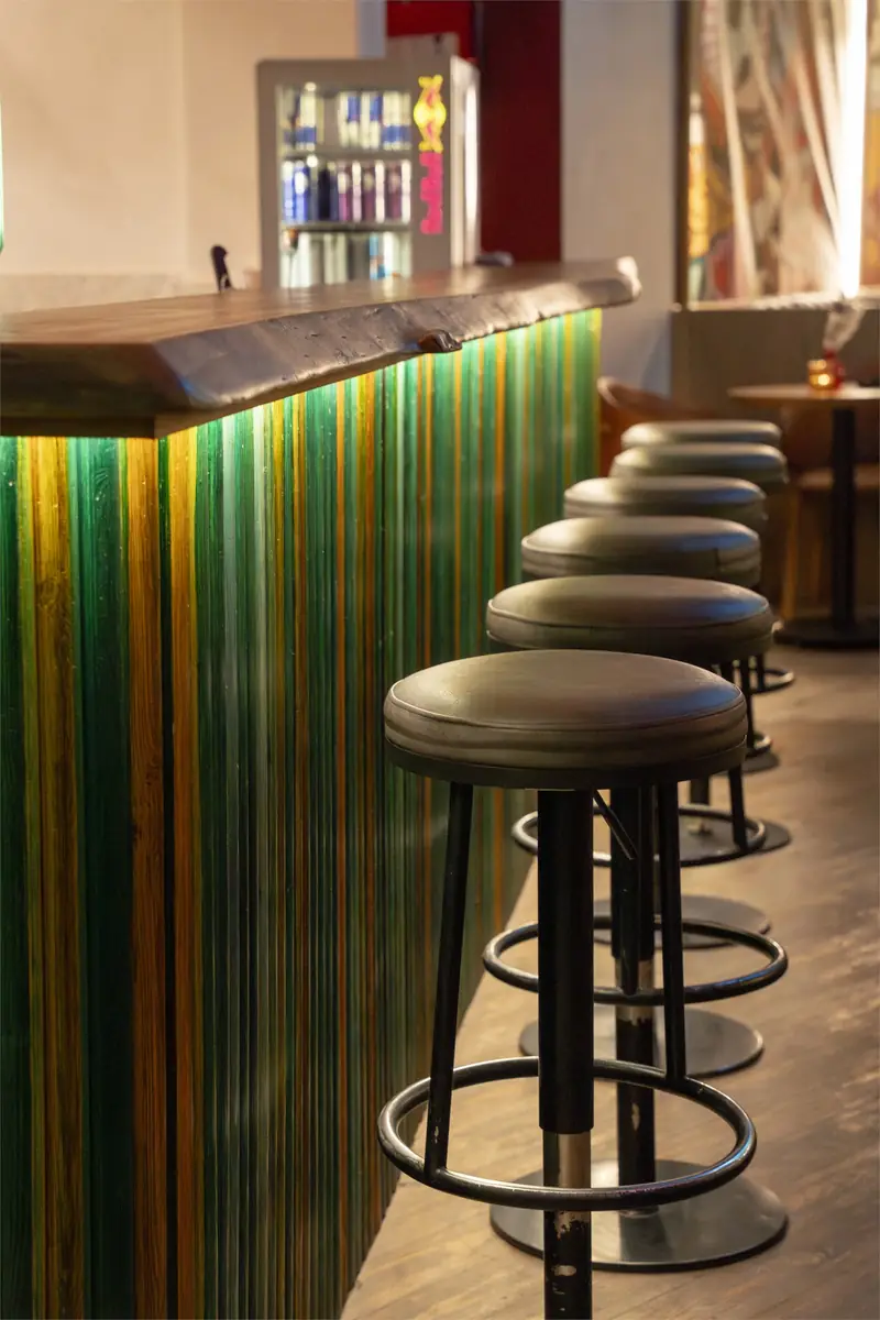Rush – Sports Bar – Bartheke mit Holzplatte mit Baumkante, grün-gold gestreifter Front und Lederhockern